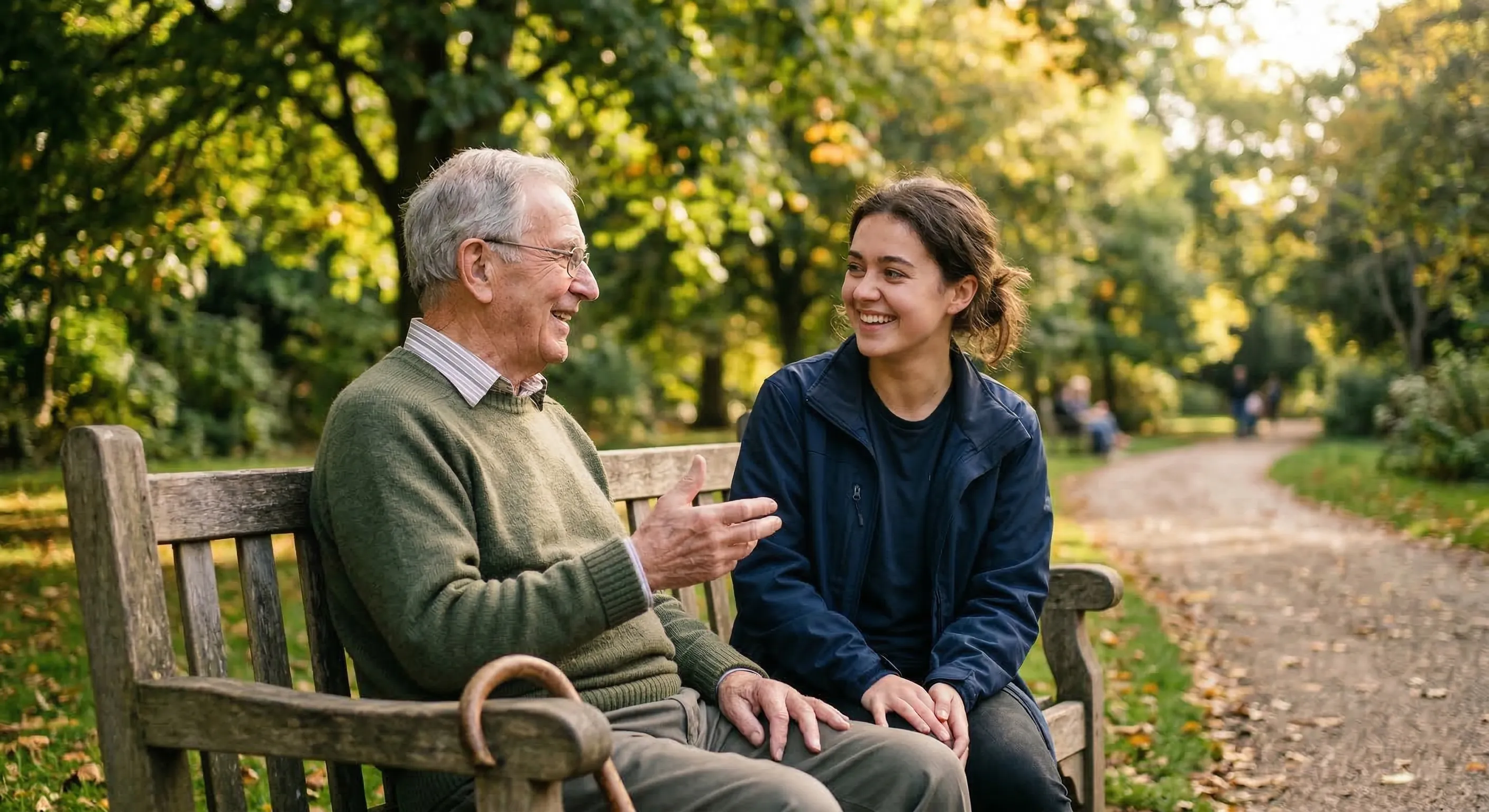 Un adulto mayor y una joven voluntaria conversan animadamente sentados en una banca de parque durante una sesión del proyecto Puentes de Papel